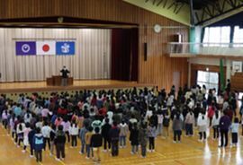 体育館に整列して先生の話を聞いている生徒たちを後ろから撮影した写真