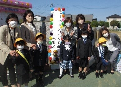 こじゅりんこども園の校門で入園の記念撮影をする5組の親子の写真