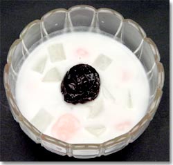 ガラスの器に盛り付けられ中央にブルーン、1センチ角のかぶと淡いピンク色の白玉がココナッツミルクの中に入っているかぶと白玉のお汁粉の写真