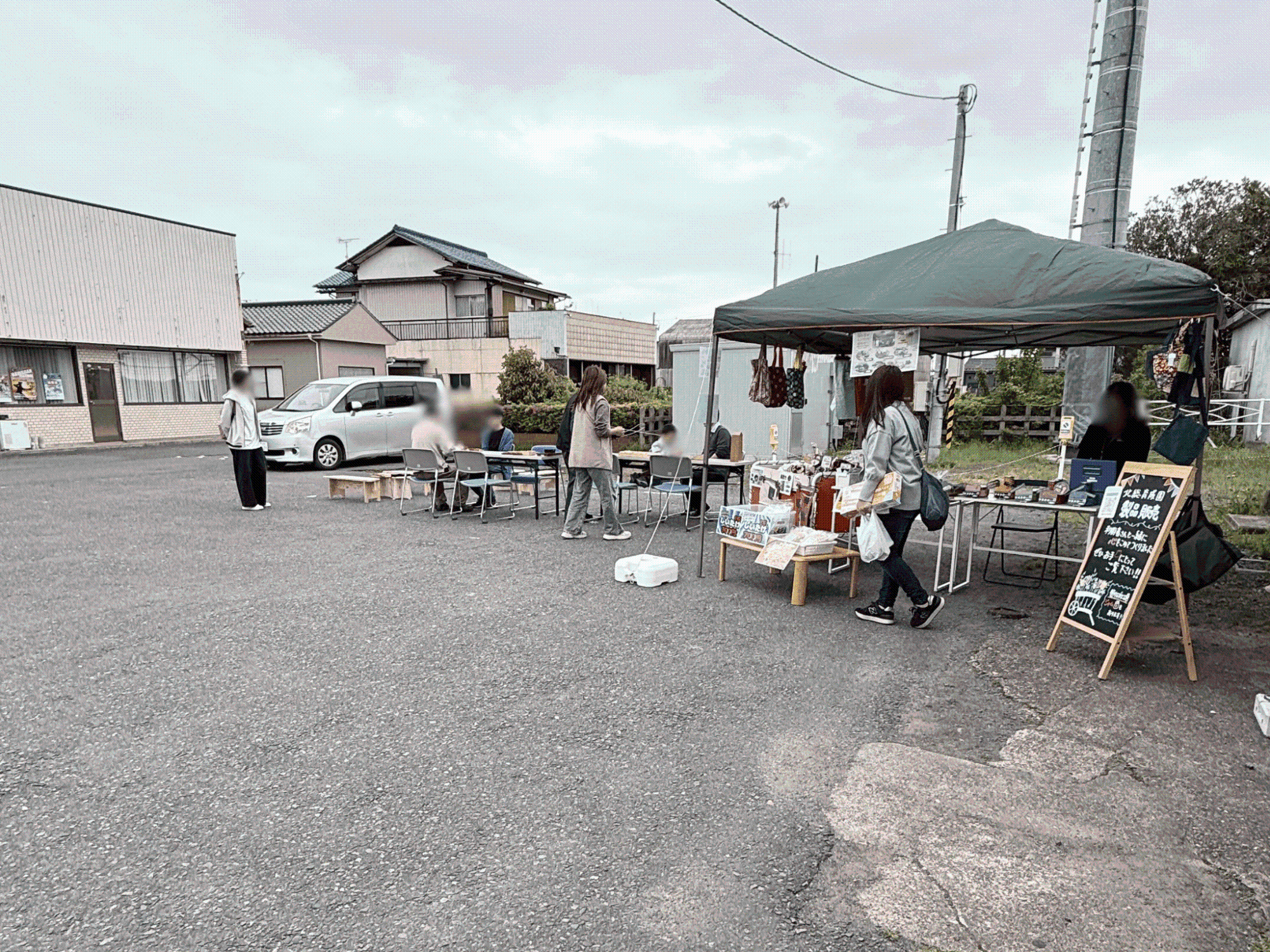笹川駅前のスペースに机を並べて将棋を楽しむ人たちの隣でテント内で物品販売も行われている様子
