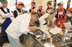 調理台の上で講師の先生が料理をしている所を参加者の人達が見ている写真